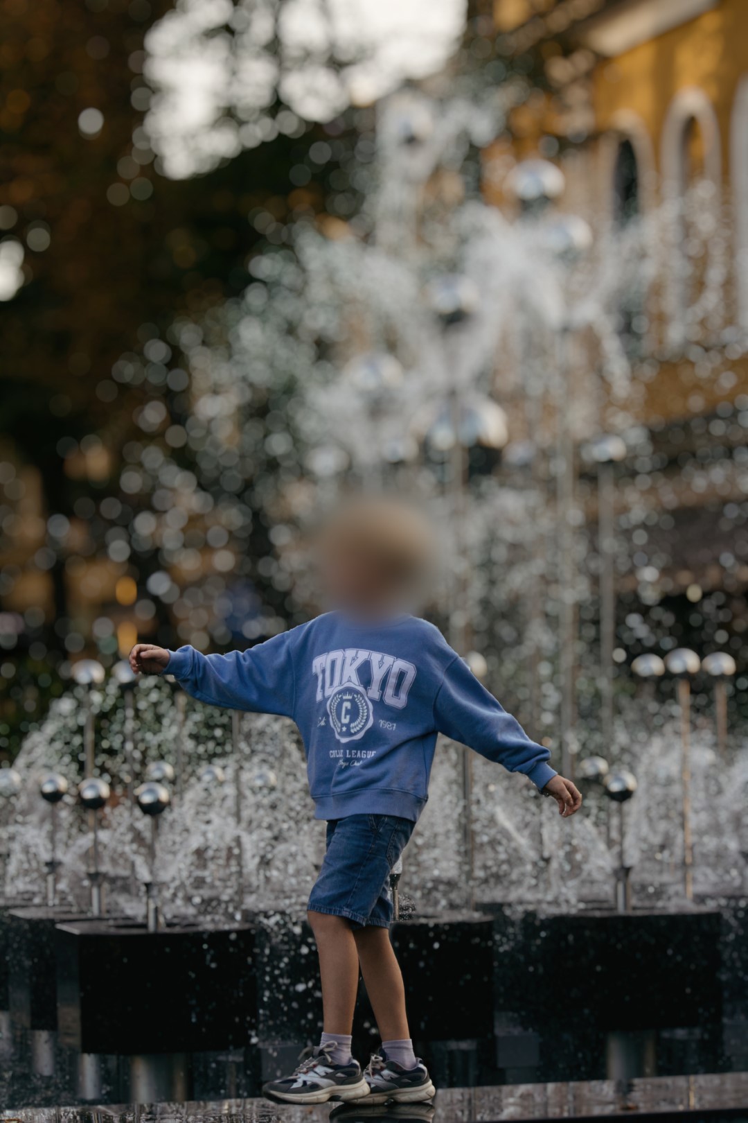 A photo of a young boy cheerfully hopping along a fountain